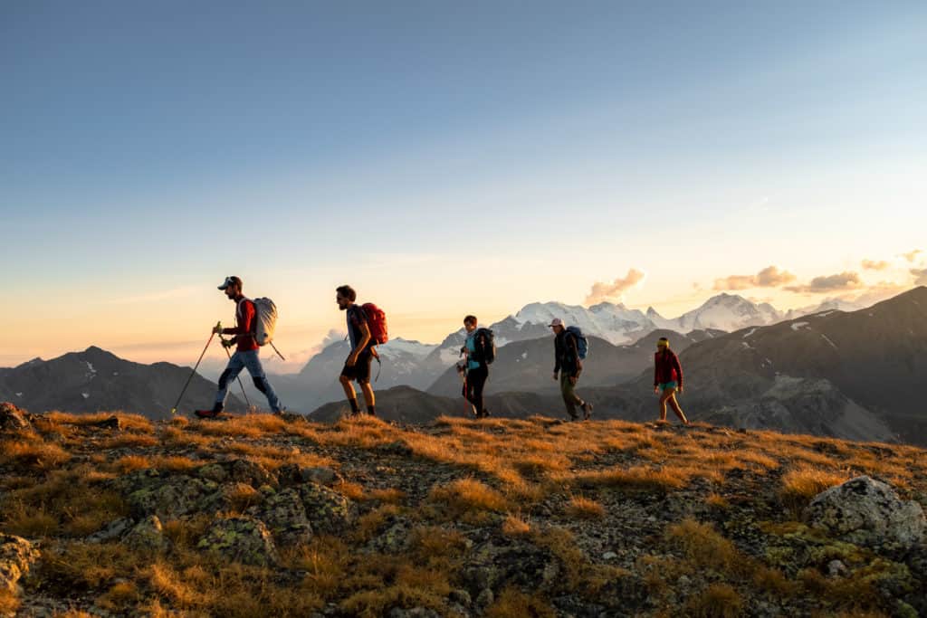 Cinque escursionisti in fila su una cresta al tramonto con cime innevate sullo sfondo: la stagione outdoor in autunno