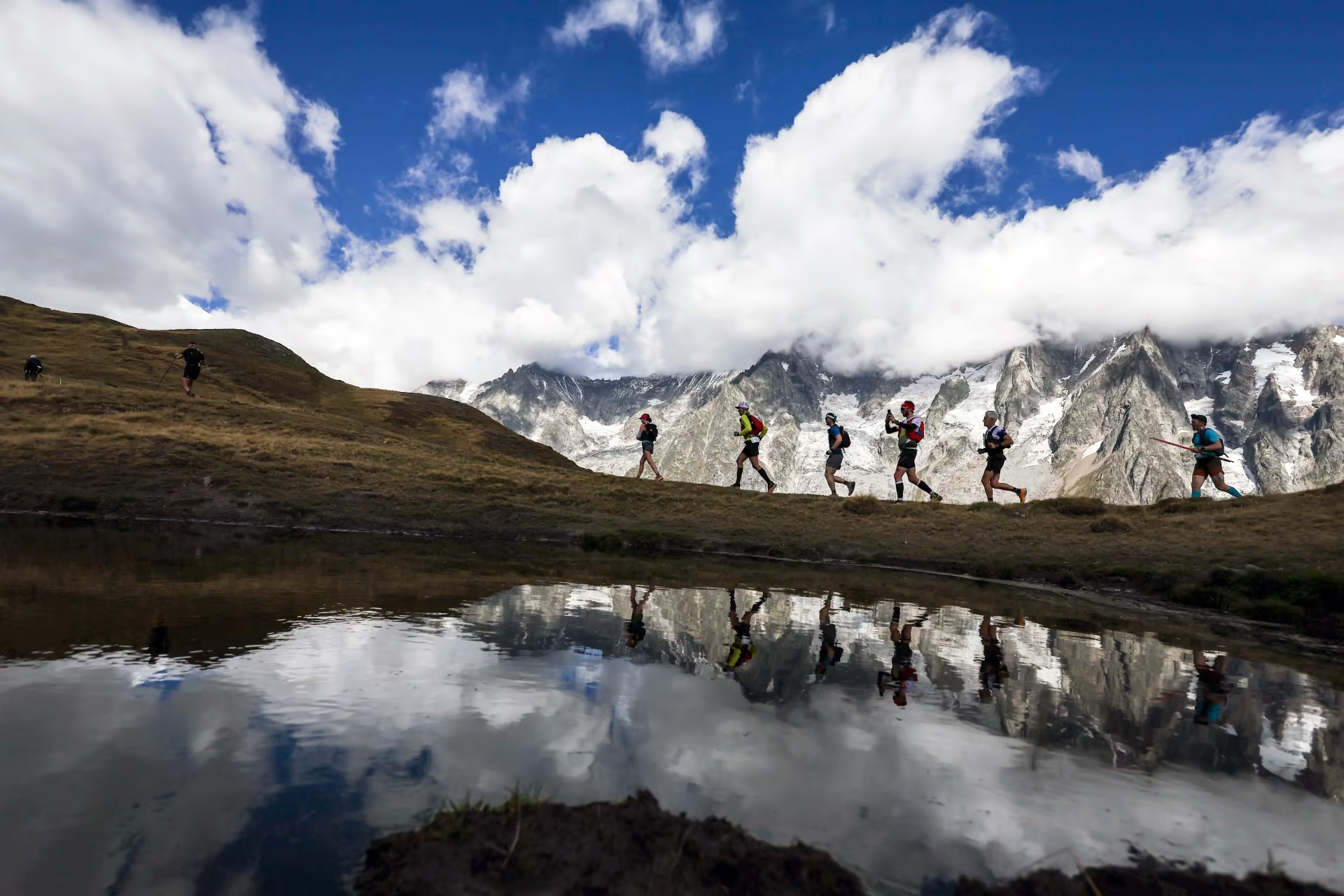Un gruppo di atleti impegnati lungo il tracciato UTMB, con le Alpi sullo sfondo