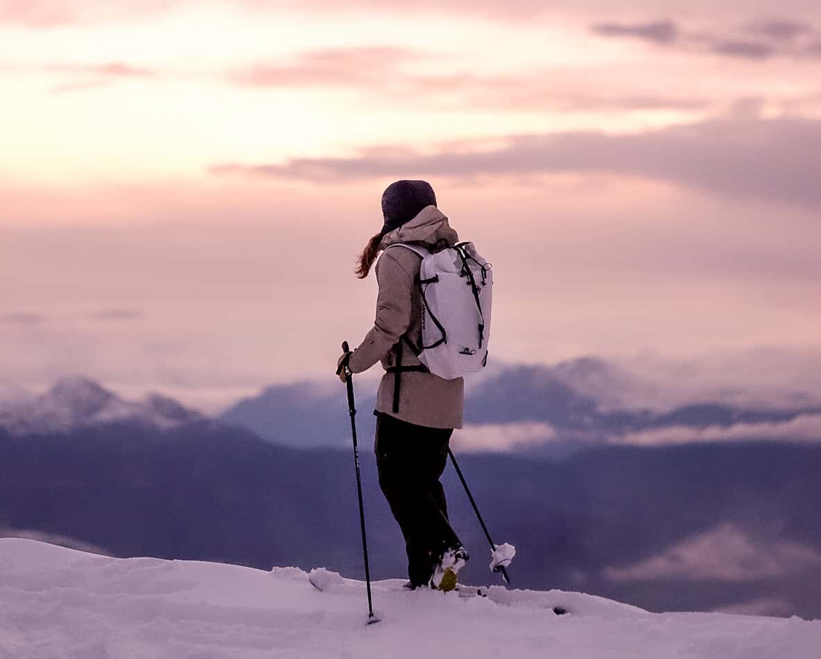 Scialpinista in salita all’alba su un crinale innevato, con panorama montano sullo sfondo, durante un’uscita di sci alpinismo