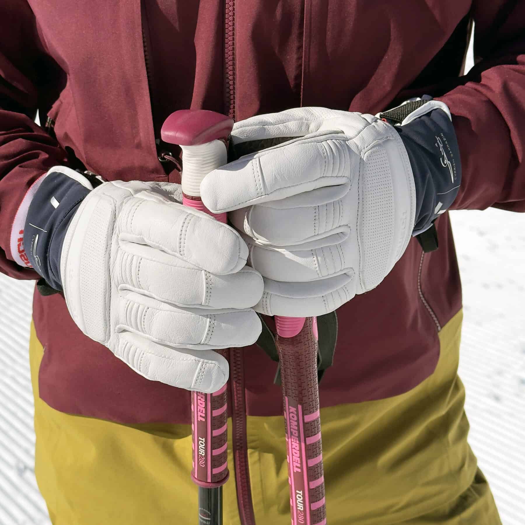 Dettaglio di guanti da sci alpino racing bianchi mentre impugnano i bastoni su pista battuta.