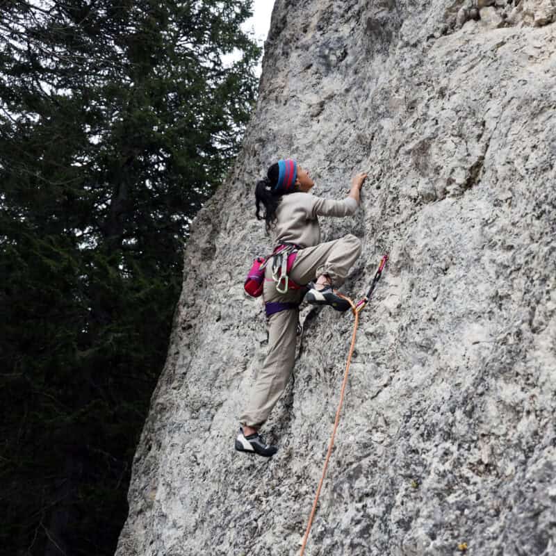 Climber donna in arrampicata sportiva su falesia di calcare con imbrago, chalk bag e scarpette tecniche — area scalare estate 2026 Outdoortest