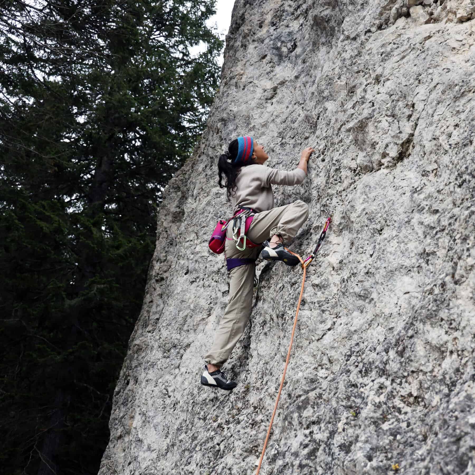 Climber donna in arrampicata sportiva su falesia di calcare con imbrago, chalk bag e scarpette tecniche — area scalare estate 2026 Outdoortest