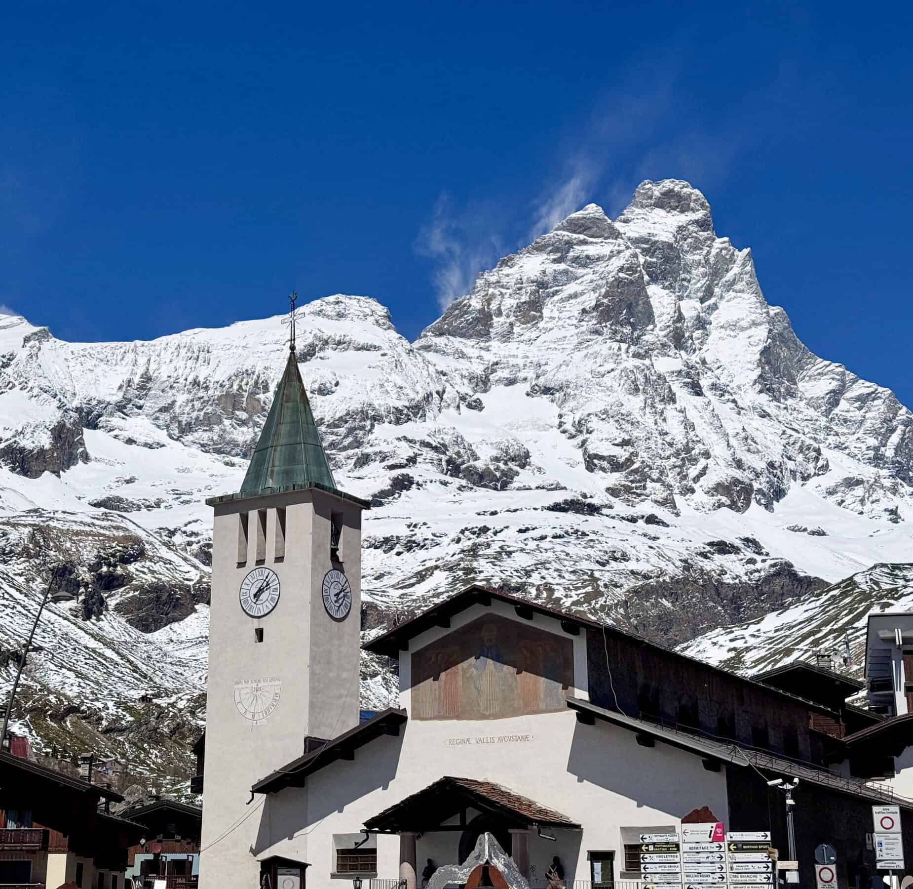 Campanile con orologio e affresco della chiesa di Cervinia con il Cervino innevato sullo sfondo