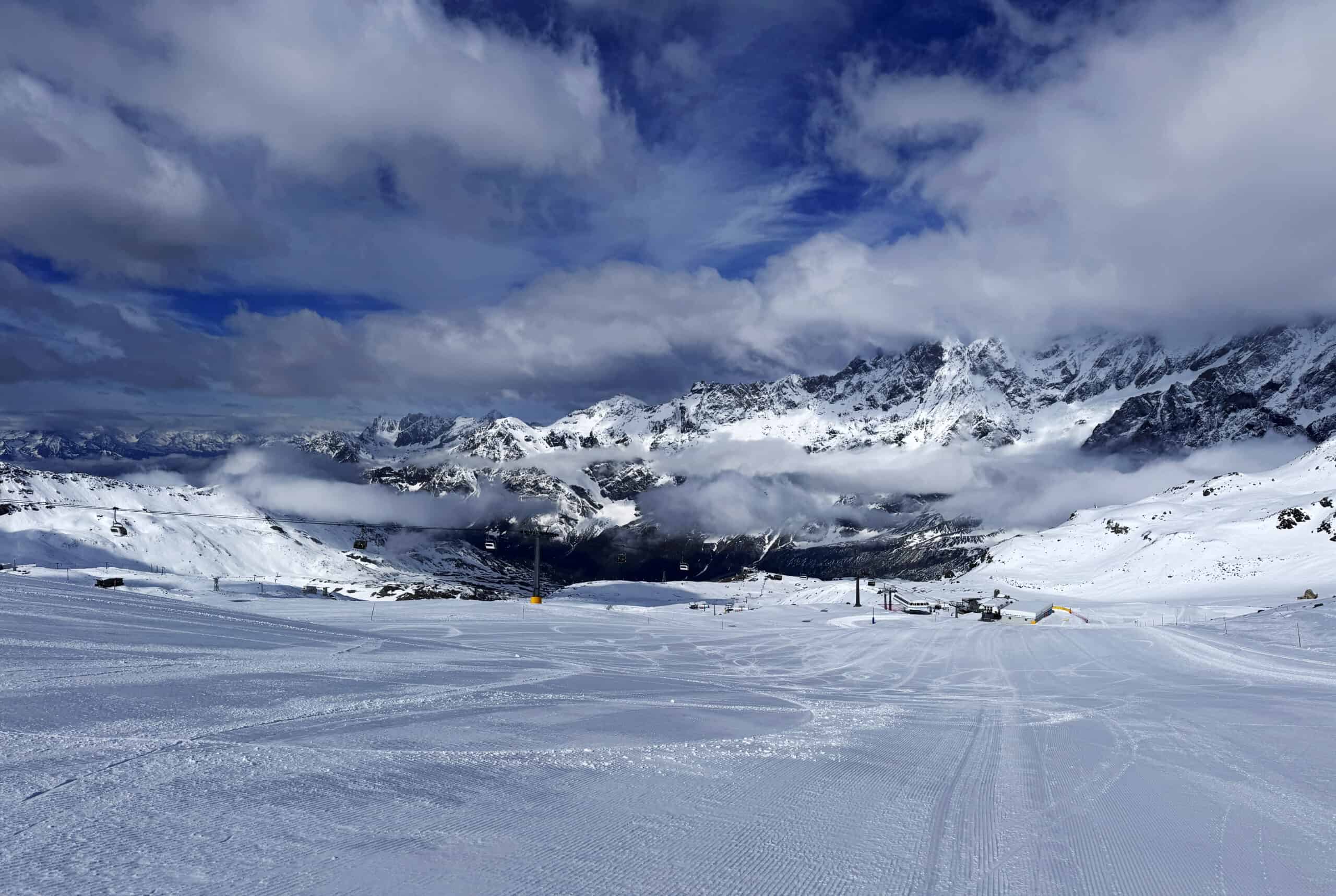 Pista del Bontadini a Cervinia completamente innevata a quota 2700 m, con gli impianti di risalita e la catena alpina sullo sfondo tra le nuvole