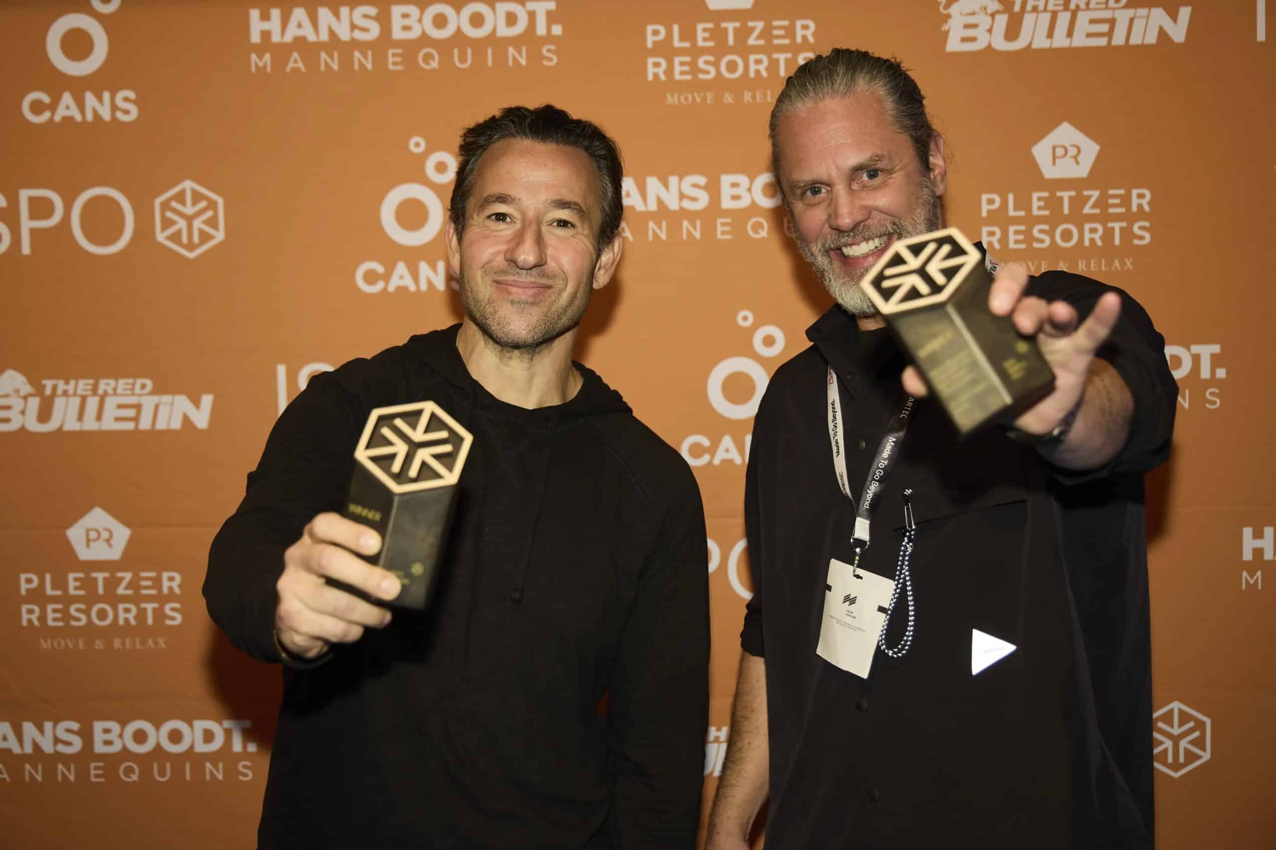 Due vincitori degli ISPO Excellence Awards 2026 mostrano il loro trofeo davanti al backdrop ufficiale della cerimonia ISPO ad Amsterdam