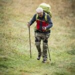 Escursionista con zaino e bastoncini in cammino su un prato in pendenza a Prato Valentino con l'esoscheletro per le anche DNSYS X1 Lite